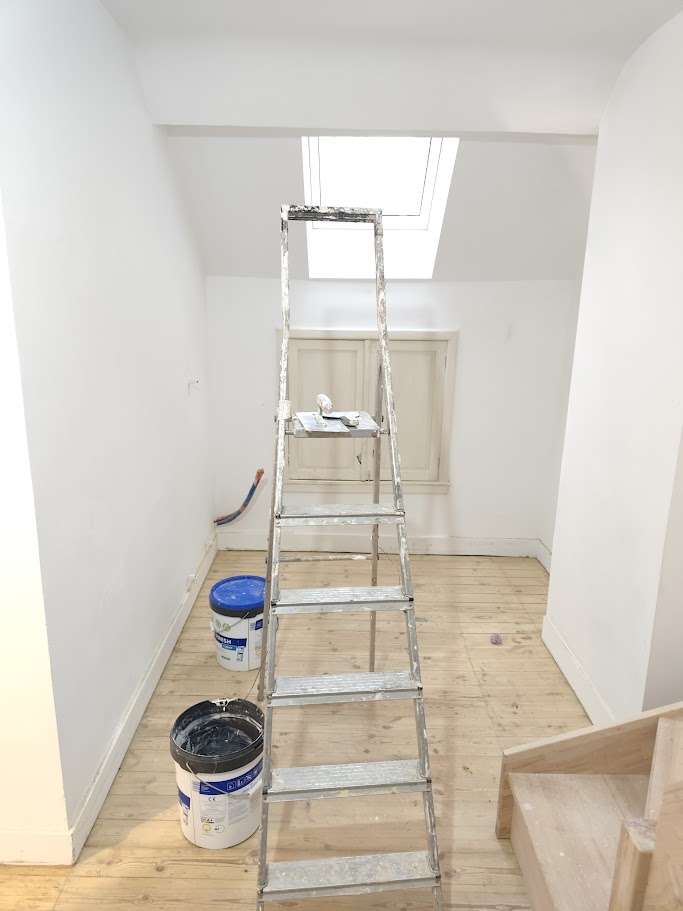 Même pièce en cours de rénovation, murs remis à neuf et parquet poncé avec escabeau et pots de peinture.