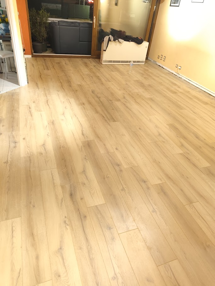 Sol de salon entièrement rénové avec nouveau parquet bois clair, vue sur la même baie vitrée une fois les travaux terminés.