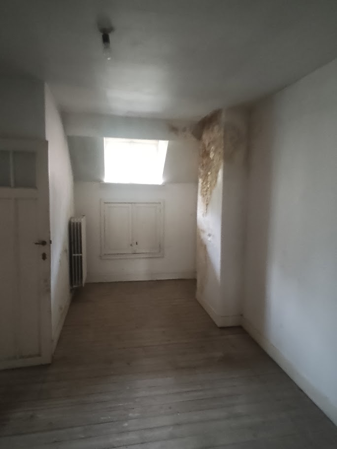 Pièce avant rénovation avec parquet ancien, murs abîmés et traces d’humidité près de la fenêtre de toit.
