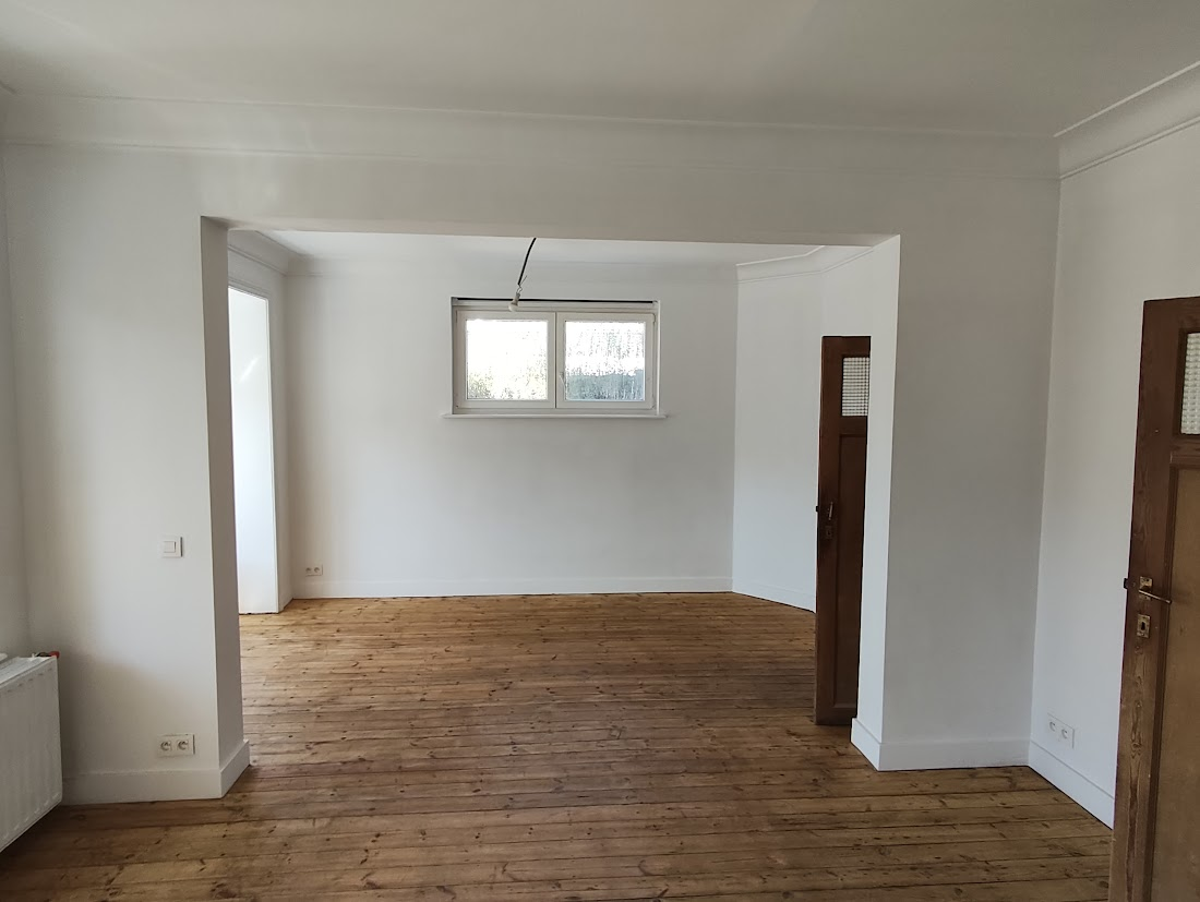 Une pièce vide avec un plancher en bois, des murs blancs et une fenêtre.