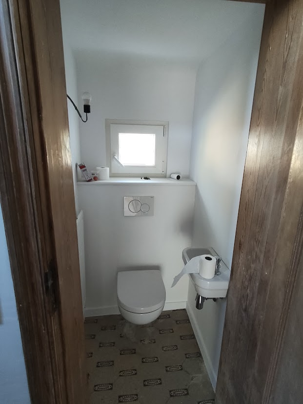 L'image montre une petite salle de bains avec un toilette, un lavabo et un petit meuble de rangement.